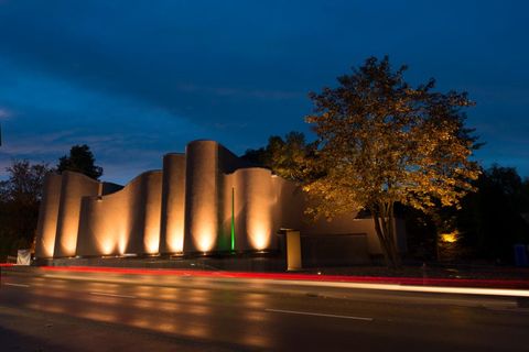 Das geschwungenge, erdfarbene und beleuchtete Gebäude des MAC Museum Art & Cars, das von von seiner Architektur den Hohentwiel und die Burgruinie darstellen soll,  von der Außanansicht von Richtung Schaffhauser Straße  (© MAC Museum Art & Cars Singen)