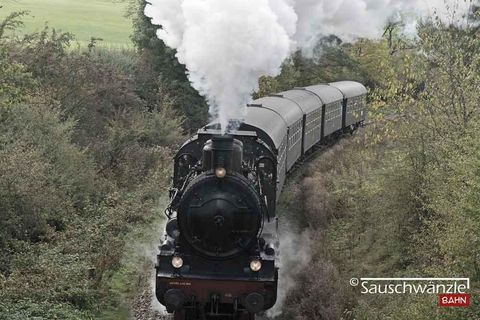 Die nostalgische Sauschwänzlebahn fährt stilgerecht mit einer historischen Dampf- und Diesellok mit fünf, schwarzen Waggons auf Schienen durch die Landschaft. Aus dem Schornstein der Lok steigt viel weißer Rauch auf. (@Sauschwänzlebahn)